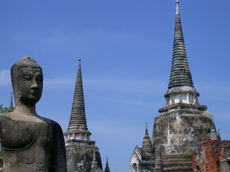 A Buddha statue with two of the three stately chedis in the background.